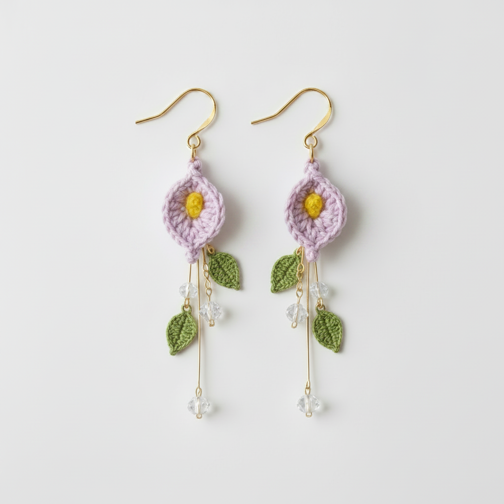 A pair of handmade crochet dangle earrings featuring light purple flower petals with yellow centers, green leaves, and gold-tone hooks, shown on a plain light gray background.
