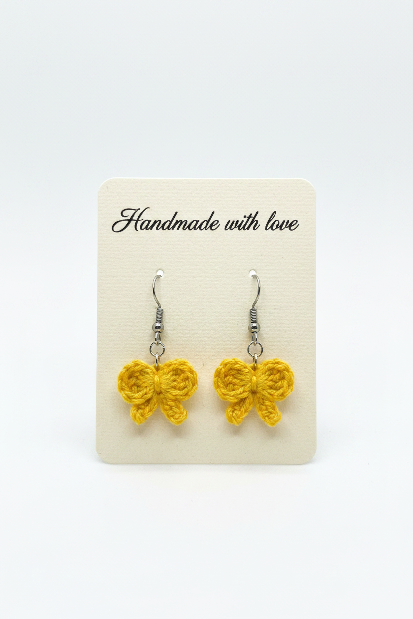 A pair of yellow crocheted bow dangle earrings on a cream display card that reads 'Handmade with love' against a white background.
