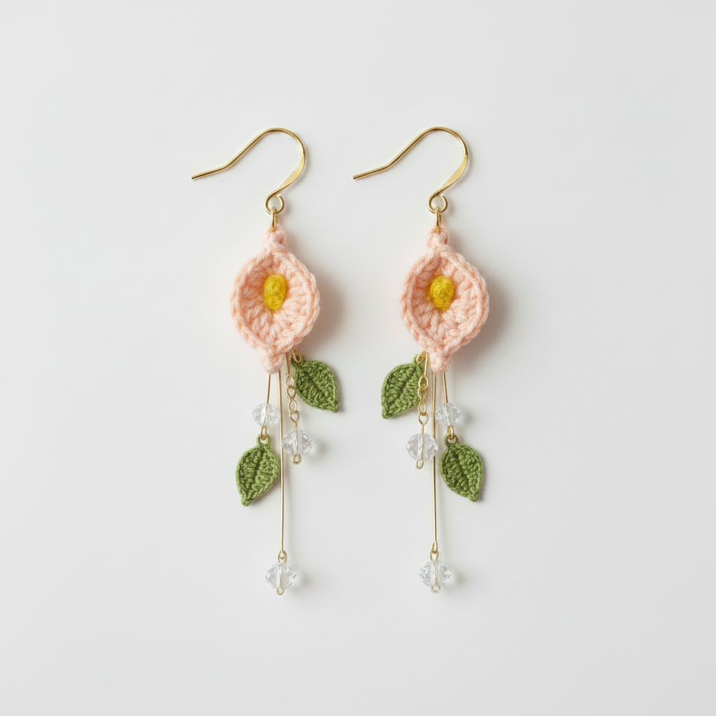 A pair of handmade crochet dangle earrings featuring light pink flower heads with yellow centers, green leaves, and gold-tone hooks, shown on a plain light gray background.