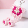 A crocheted butterfly-shaped keychain charm in light pink with bright pink and cream centers, attached to a silver metal ring, shown on a soft pink and white background with two small matching crocheted flower pieces below.