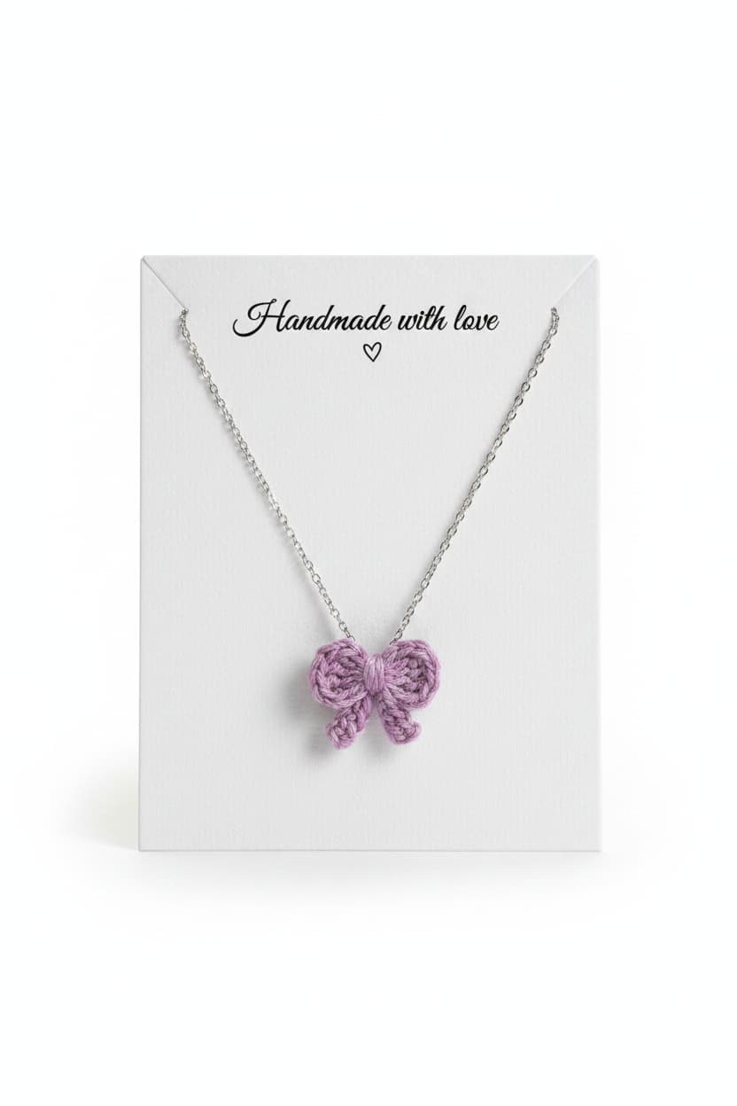 A silver chain necklace with a knitted lavender-purple bow pendant, displayed on a white gift card that reads 'Handmade with love'.