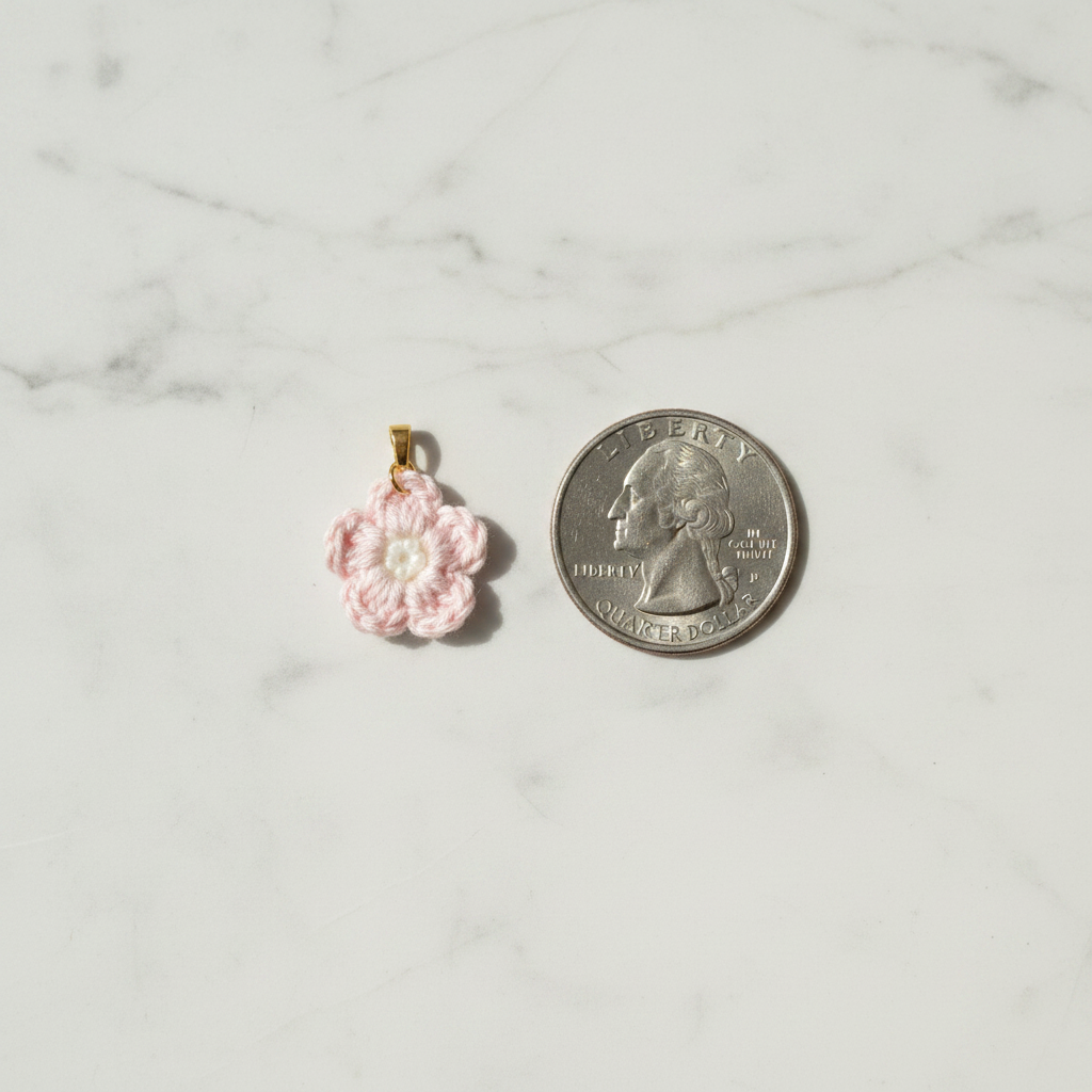 A small pink crocheted flower charm with a gold-tone loop at the top, shown next to a U.S.
