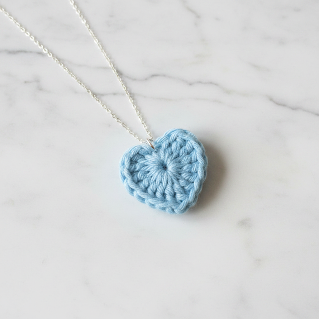 Crocheted heart pendant on a chain against a marble background