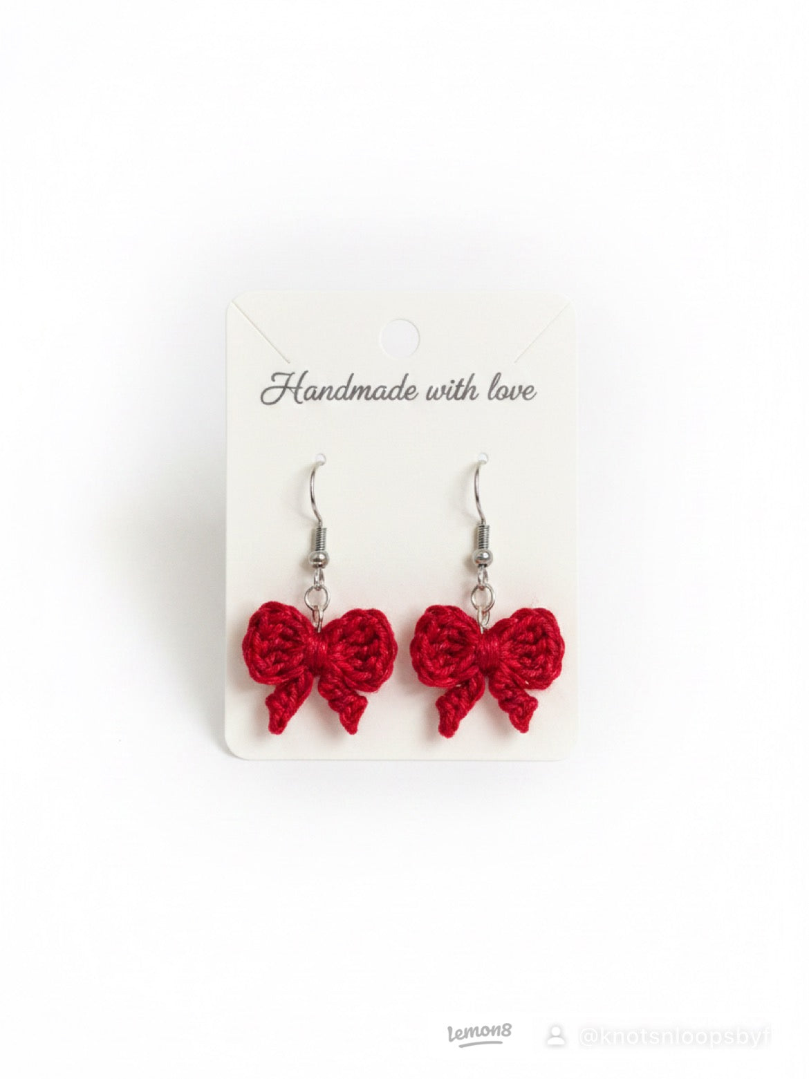 A pair of handmade red crocheted bow drop earrings on a white display card that reads 'Handmade with love'.