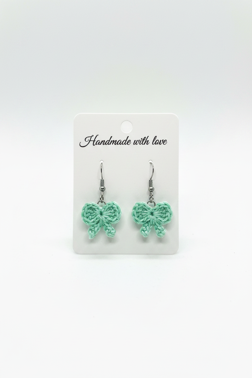 A pair of handmade mint green crocheted heart-shaped dangle earrings on a white display card that reads 'Handmade with love' against a white background.