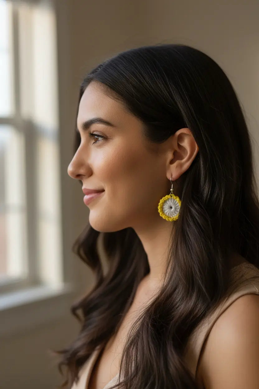 A woman in profile wearing a yellow and white dangle earring with a clock face design, set against a soft-focus indoor background.