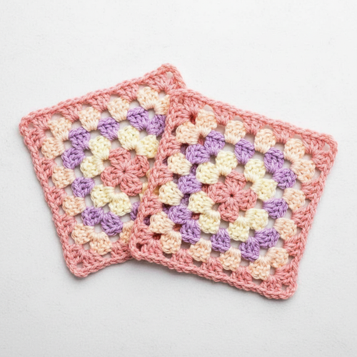 Two handmade crocheted square coasters with a colorful granny square pattern in pink, purple, and cream, displayed on a light gray background.