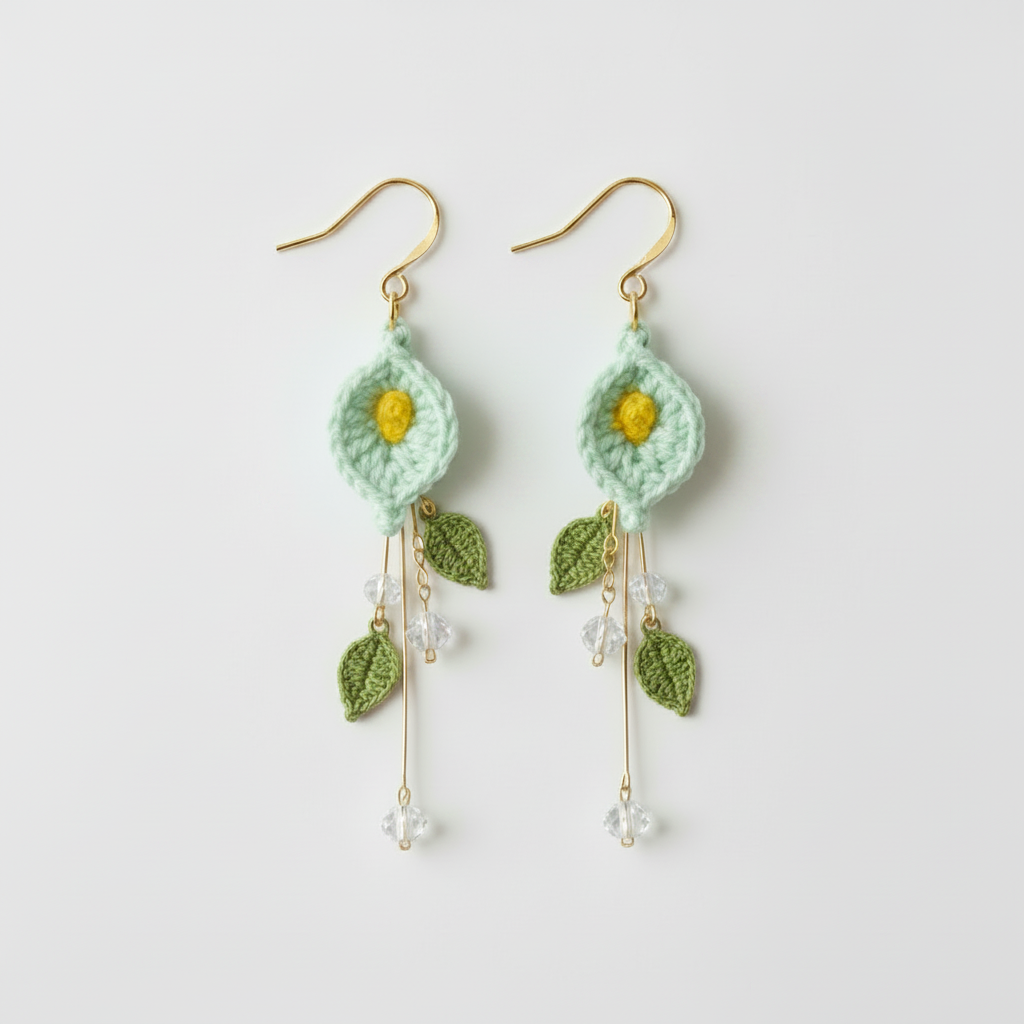 A pair of handmade crochet dangle earrings featuring mint green flower petals with yellow centers, green leaves, and gold-tone hooks with clear crystal beads.