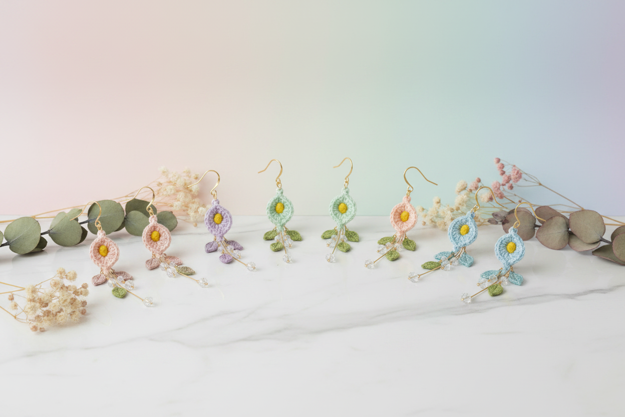 A set of handmade floral dangle earrings displayed on a white marble surface with decorative dried flowers and greenery. The earrings feature gold-tone hooks and frames in pastel pink, lavender, mint green, peach, and light blue, with small yellow flower centers and green leaf details.