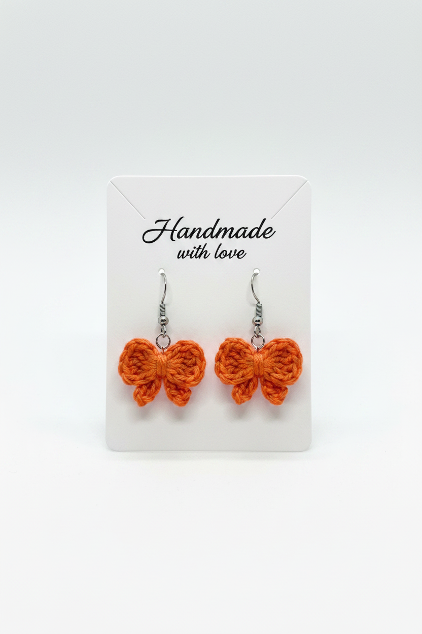 A pair of handmade orange crocheted butterfly earrings on a white display card that reads 'Handmade with love'.