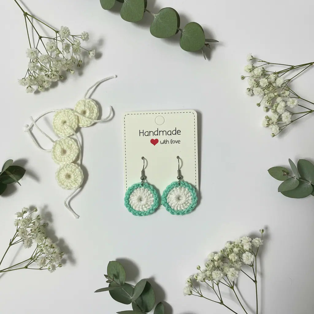 A pair of handmade crocheted dangle earrings displayed on a cream card that reads 'Handmade with love'. The earrings feature a mint green and white crochet pattern.