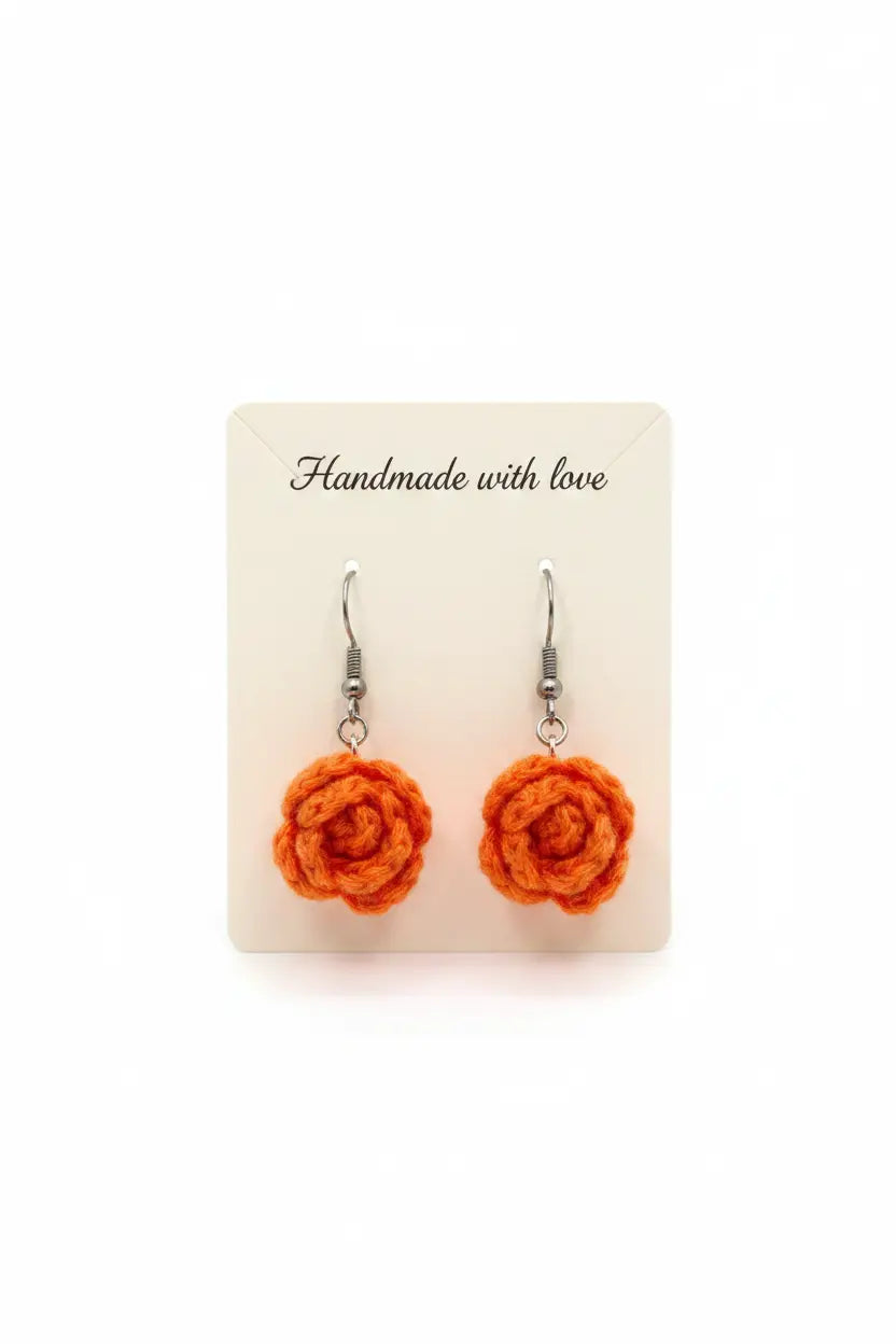 A pair of handmade orange crochet rose dangle earrings on silver fishhook wires, displayed on a cream-colored backing card that reads 'Handmade with love'.