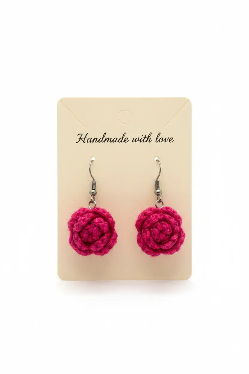 A pair of handmade pink crochet flower dangle earrings on a beige display card that reads 'Handmade with love' against a white background.