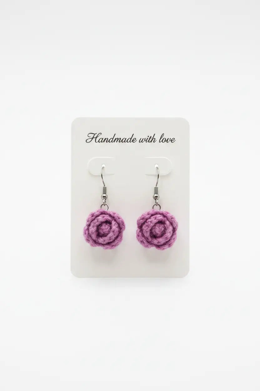 A pair of handmade purple crochet rose dangle earrings on a white display card that reads 'Handmade with love' against a white background.