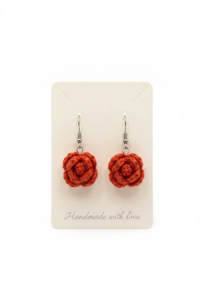 A pair of handmade orange crochet rose drop earrings with silver fishhook wires, displayed on a cream-colored backing card that reads 'Handmade with love'.