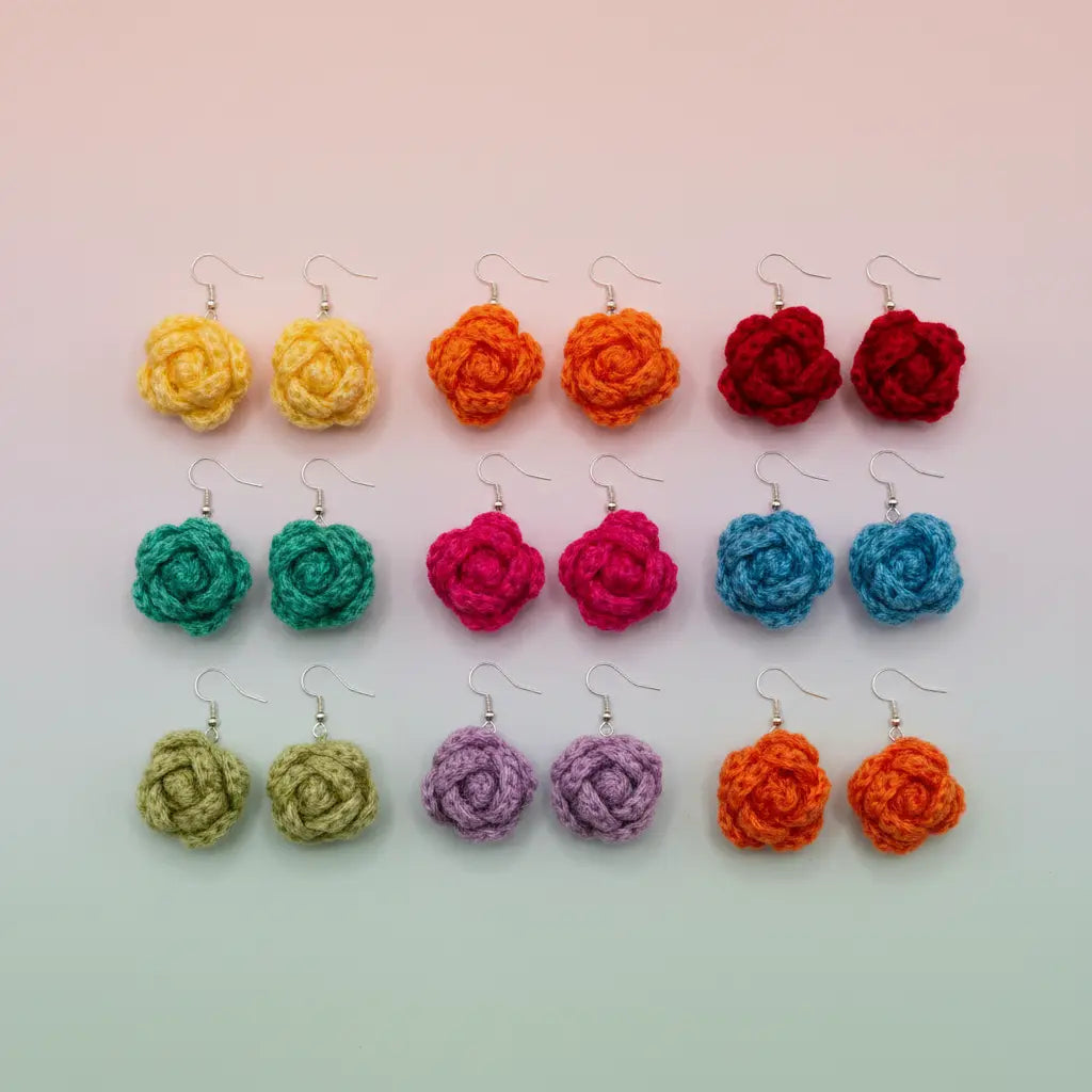 Six pairs of handmade crocheted rose earrings arranged in a grid on a pastel gradient background. The colors include yellow, orange, red, green, pink, blue, light green, purple, and a second orange.