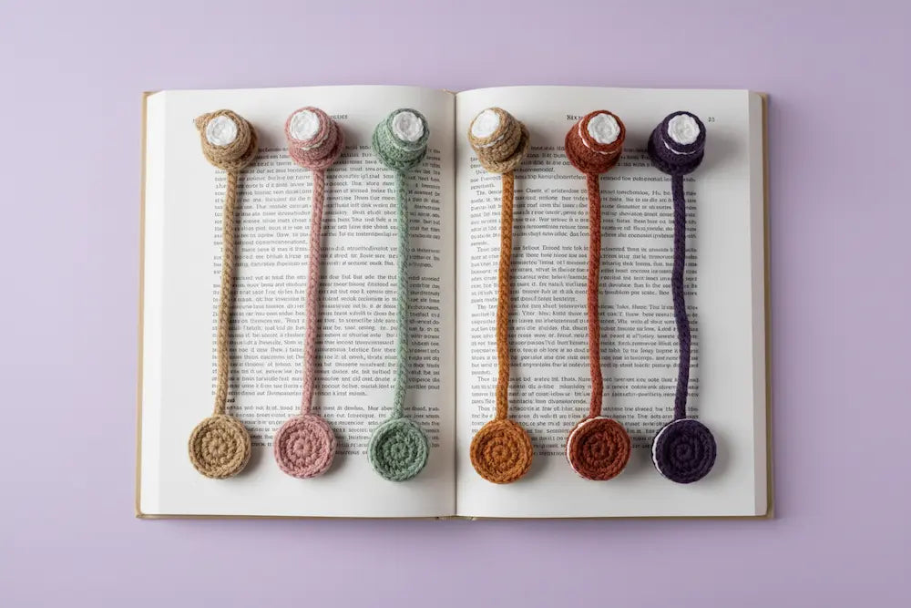 Six handmade crocheted bookmarks in earthy colors are arranged on the pages of an open book, set against a solid light purple background.