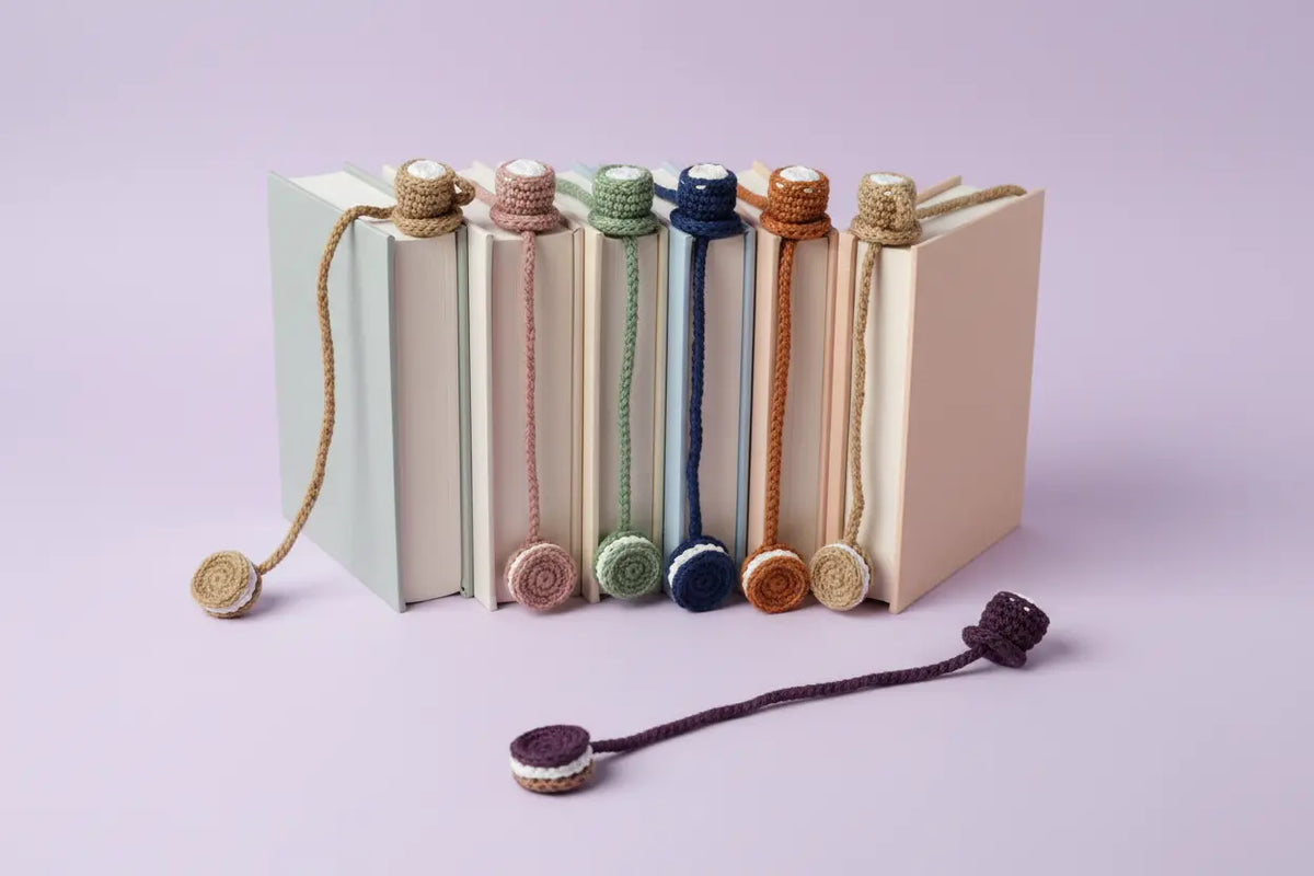 A set of handmade crochet bookmarks with round woven discs, shown tied around the spines of several books on a light lavender background, with one bookmark displayed in front.