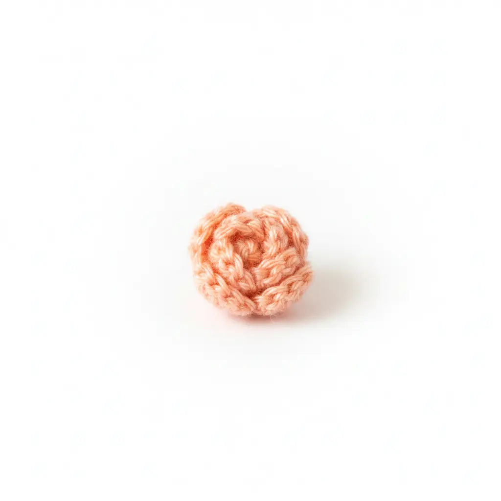 A small crocheted peach-pink flower rosette, likely made from yarn or thread, centered on a clean white background.