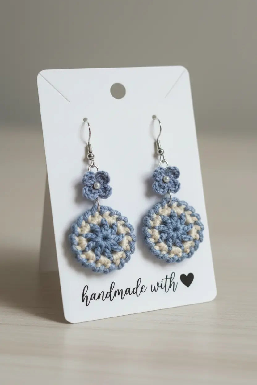 A pair of handmade crochet dangle earrings in light blue and cream, displayed on a white card that reads 'handmade with a heart'.