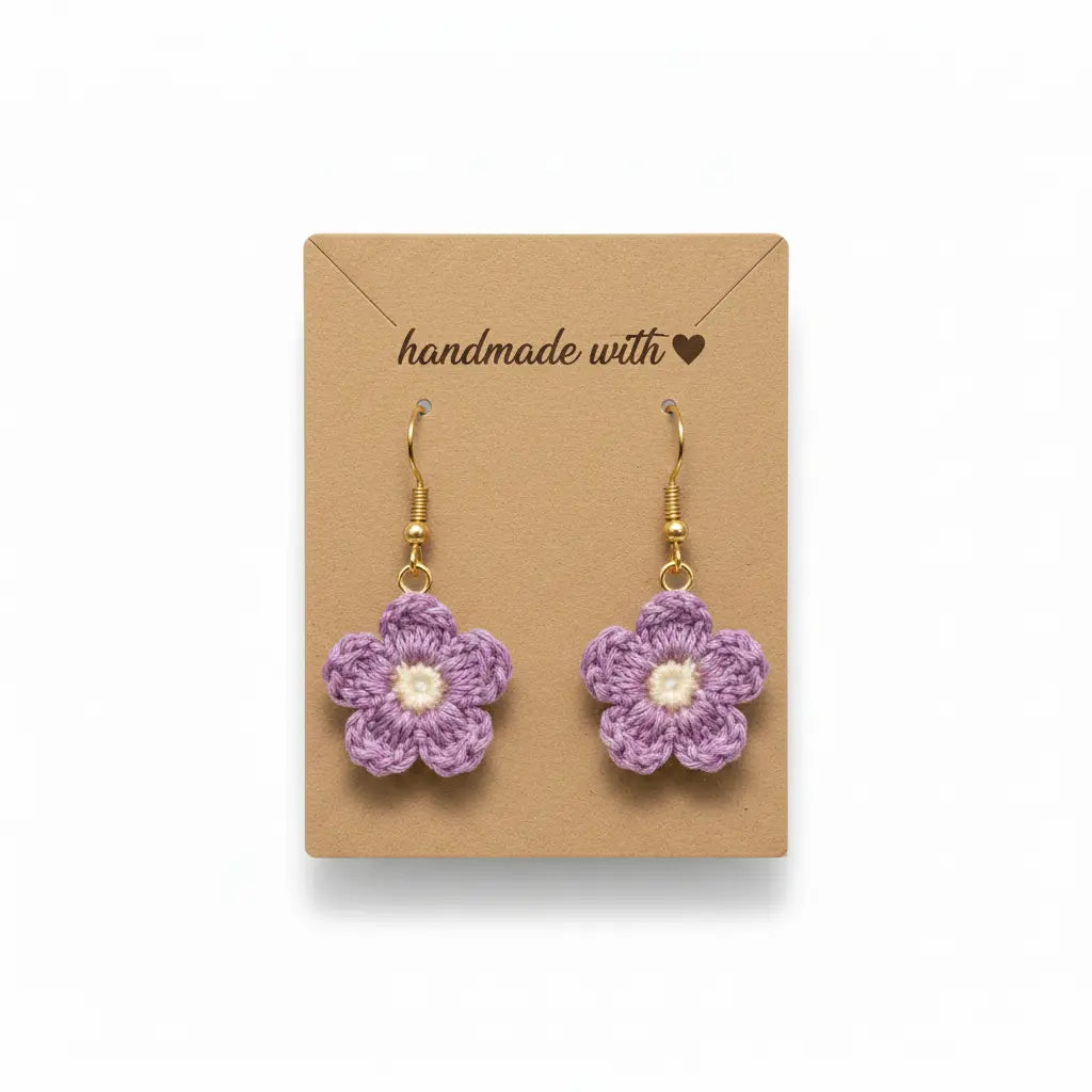 A pair of handmade purple crocheted flower dangle earrings with gold hooks and cream centers, displayed on a brown kraft paper card that reads 'handmade with a heart'.