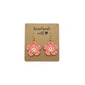 A pair of handmade crocheted flower drop earrings in pink with white centers and gold hooks, displayed on a brown kraft card that reads 'handmade with a heart'.