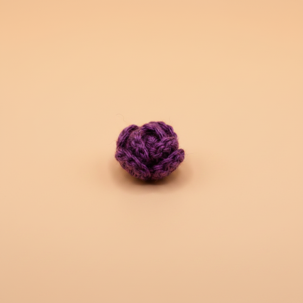 A small purple crocheted or knitted rosette flower accessory, centered on a solid warm beige background.